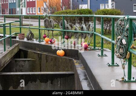 Round marker buoys in orange and dark red and coiled ropes hang on the green railing. Stock Photo