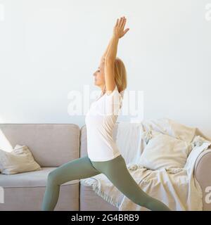 Focused retired mature women in sports wear practicing Warrior Yoga Pose at home Stock Photo