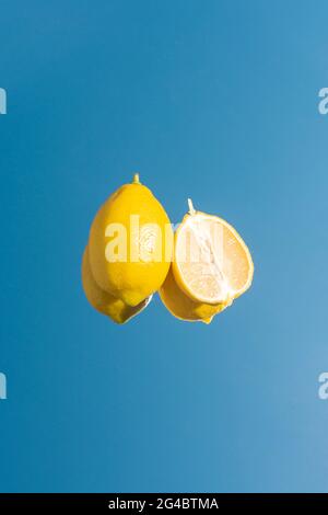 Still life of whole lemon and lemon wedge on mirror, reflecting blue sky. Isolated yellow lemon on blue background. Stock Photo