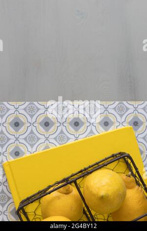 Some lemons inside a black metallic wire basket on a yellow book over a hydraulic geometric floor with some copy space at the top of the image. Stock Photo