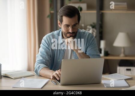 Concentrated happy young business man working on computer at home. Stock Photo