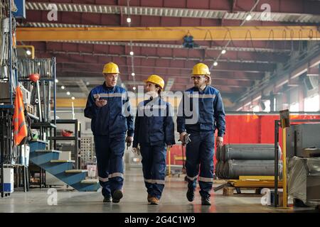 Mature factory foreman walking along workshop and gesturing hand while explaining tasks to employees in industry Stock Photo