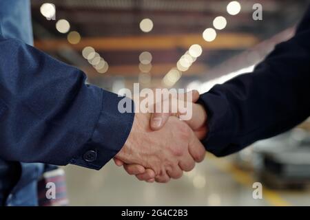 Close-up of unrecognizable factory executives making handshake in industrial shop with lights Stock Photo
