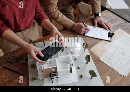 Directly above view of unrecognizable assistant photographing 3D model of house while architect making notes about room space Stock Photo
