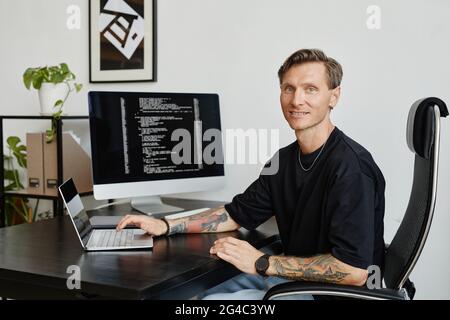 Portrait of mature computer programmer smiling at camera while working at the table with computers Stock Photo