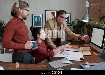 Team of multi-ethnic architectural engineers looking at computer monitor and discussing house structure while elaborating it Stock Photo