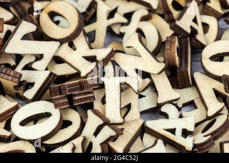 A stack of small wooden letters on a dark table. Letters outlines for arranging inscriptions and words. Dark background. Stock Photo