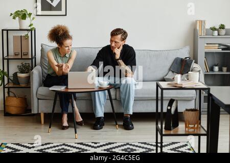 Two business people sitting on sofa using laptop and discussing online presentation at office Stock Photo