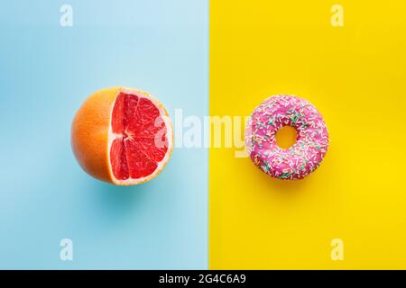 Healthy and unhealthy food, Flat layer, Two color background, Pink donuts on yellow, juicy grapefruit on pastel blue, cut into half Stock Photo