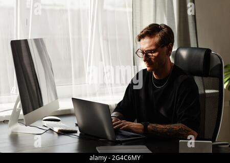 Serious programmer working on laptop at the table and developing new software at developing company Stock Photo