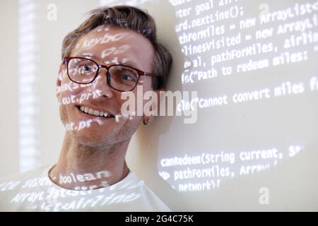 Portrait of young IT manager smiling at camera leaning on the white wall with computer code Stock Photo