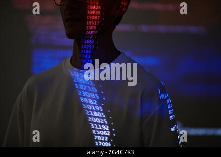 Young computer hacker with computer code reflecting on his face working in dark room Stock Photo