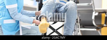 Rehabilitation doctor helping to lift leg of patient in wheelchair closeup Stock Photo