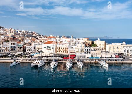 Syros island, Greece, aerial drone view. Sailboats moored at yachts port dock. Ermoupolis town buildings, blue sky background. Boats reflection on cal Stock Photo