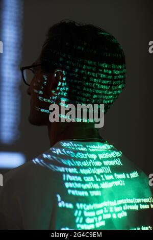 Rear view of computer hacker sitting and reading a computer code reflecting on his back Stock Photo