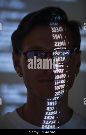 Close-up of computer hacker in eyeglasses examining computer code with numbers reflecting on his face Stock Photo