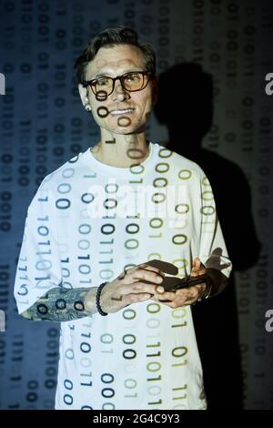 Portrait of young man in eyeglasses smiling at camera while using mobile phone in cyber security center Stock Photo