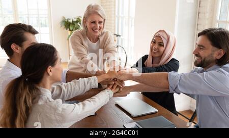 Excited smiling multiethnic employees team stacking hands at meeting Stock Photo
