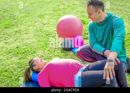 couple of a smiling personal trainer and a beautiful woman doing workout exercises outdoor. friends practicing stretching after gym session outside. Stock Photo