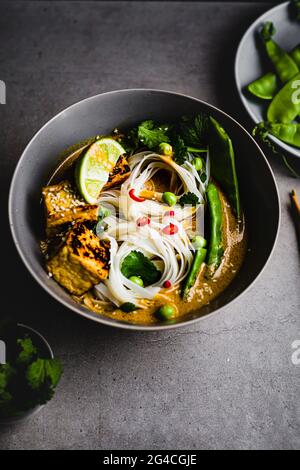 Plant based Laska noodle soup bowl with Tofu, Sweet Peas, coriander and chilli Singapore, Malaysian. Easy healthy recipe Stock Photo