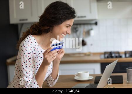 Profile of excited woman holding credit card, using laptop Stock Photo