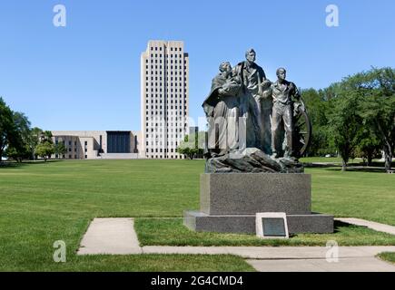 1946 bronze sculpture Pioneer Family Statue by Avard Fairbanks and the 1934 Art Deco North Dakota State Capitol building in Bismarck, North Dakota. Stock Photo
