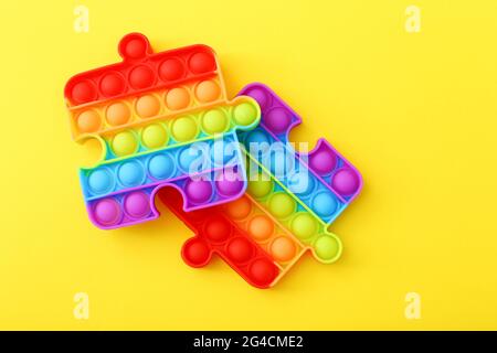 Popit toy in the form of a puzzles on a yellow background. Multicolored Pop it toy Stock Photo