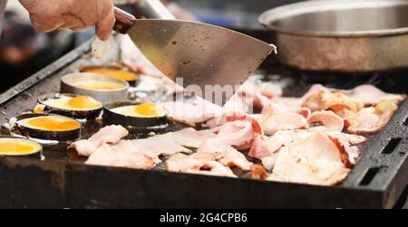 Cooking a large number of bacon and eggs on a bbq grill or hot plate. Stock Photo