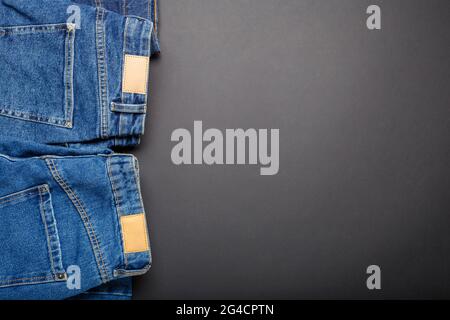 Classic blue jeans. Casual pants clothing blue jeans with brown blank leather labels on black background with copy space. Top view Stock Photo
