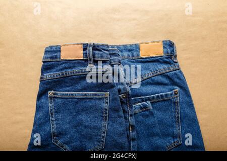 Classic blue jeans. Casual pants clothing blue jeans with brown blank leather labels on beige craft background. Top view Stock Photo