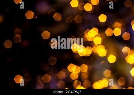 Blurred golden lights abstract background in the night, defocused dark glowing bokeh backdrop, magical yellow illuminated sparkle pattern. Stock Photo