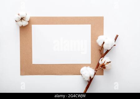 White blank paper invitation card mockup with dry bloom cotton flowers branch on flat lay. Modern desktop mock up for greeting card. Elegant working Stock Photo