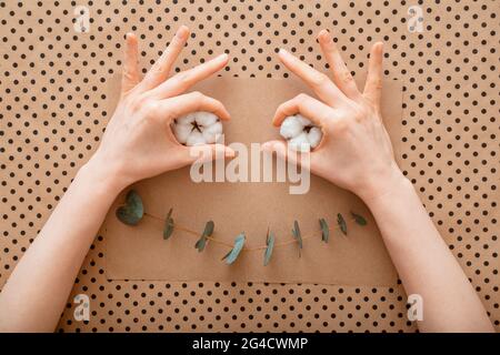 Funny cartoon face hand made from eucalyptus and cotton flowers. Muzzle face craft with female hands. Smile emotion happiness made of flowers creative Stock Photo