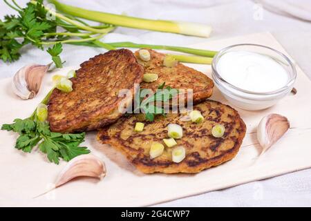 Traditional homemade vegetarian potato pancakes (draniki, raggmunk, boxty) with sour cream and greens on light background. Stock Photo