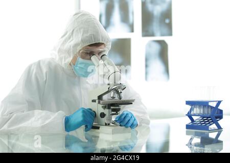 Doctor in a protective suit with gloves adjusts protective glasses near a microscope in a medical laboratory Stock Photo