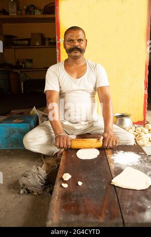Attractive Indian street seller man with big Mustache, making rolls dough balls samosa for his soap Stock Photo