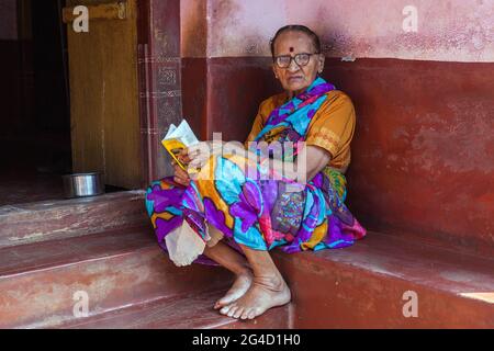 Elderly Indian female sits on porch outside her home reading book, Gokarna, karnataka, India Stock Photo