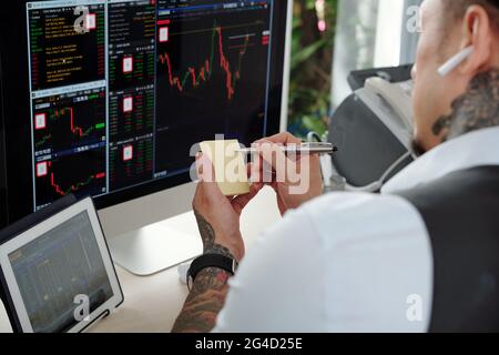 Professional trader analyzing stock market data on computer scren and taking notes on stickers Stock Photo