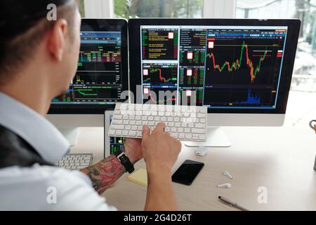 Stockbroker buying and selling shares on behalf of clients, he is looking at computer screen and pushing button on keyboard Stock Photo