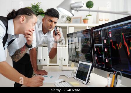 Serious worried traders analyzing indices and financial charts when trading online on cryptocurrency stock market Stock Photo