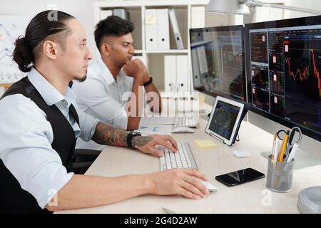 Pensive serious young traders working at office desk, analyzing stock market trends, buying and selling stocks and futures Stock Photo