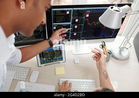 Hands of traders pointing at computer screen, analyzing and discussing stock market trends Stock Photo