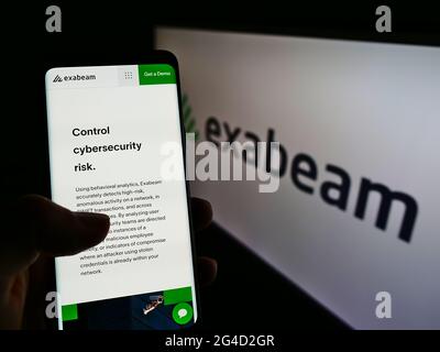 Person holding mobile phone webpage logo of US cybersecurity company Exabeam Inc. on screen in front of logo. Focus on center of phone display. Stock Photo