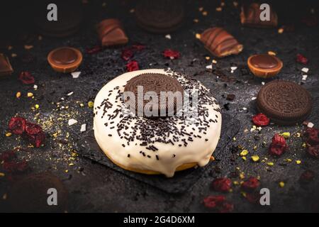 Yummy donuts with glaze, sprinkles and biscuits on black slate background Stock Photo