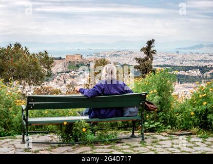 Defocused unidentified seated man enjoys the view from Lycabettus Hill. The Acropolis dominates the picture, with the Saronic gulf and Piraeus in the