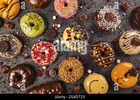 Top view of assorted donuts on black slate background. Various glazed doughnuts with sprinkles. Stock Photo