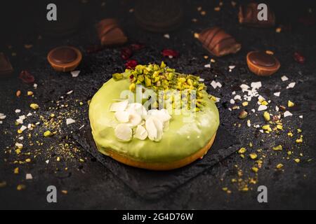 Donut in green glaze with pistachio and almond flakes on black slate background Stock Photo