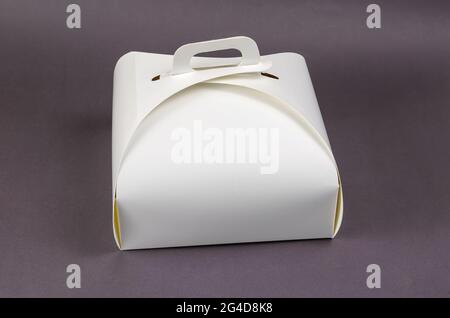 White Paper Cake or Lunch Box on Gray. Closed kraft packaging with convenient handles. Food to take away. Stock Photo