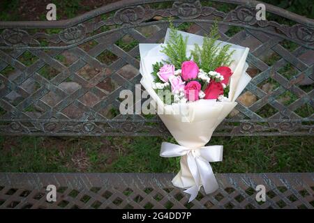 Bouquet of fresh red and pink roses rest on a rustic steel chair. Copy space. Stock Photo