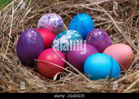 Multicolored purple and blue eggs with glitters composed in heap on straw nest for Easter holiday Stock Photo